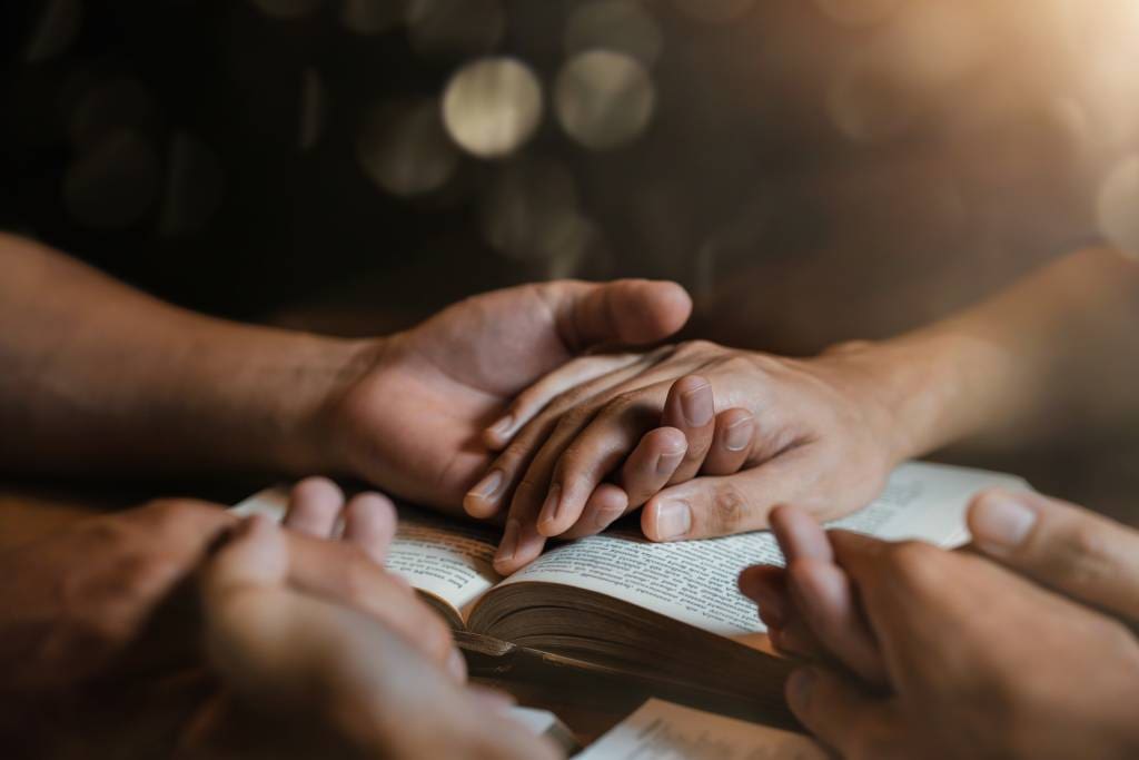 A group praying with their hands on a Bible.