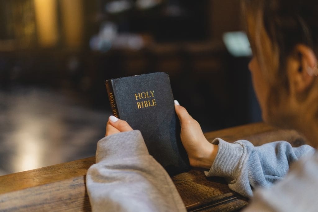 A kneeling woman holding a copy of the Bible.