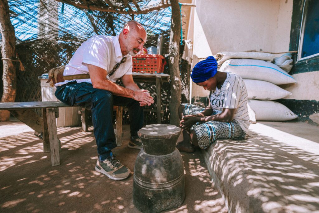 A GCR team member prays with a young believer under a shaded shelter outside her home.