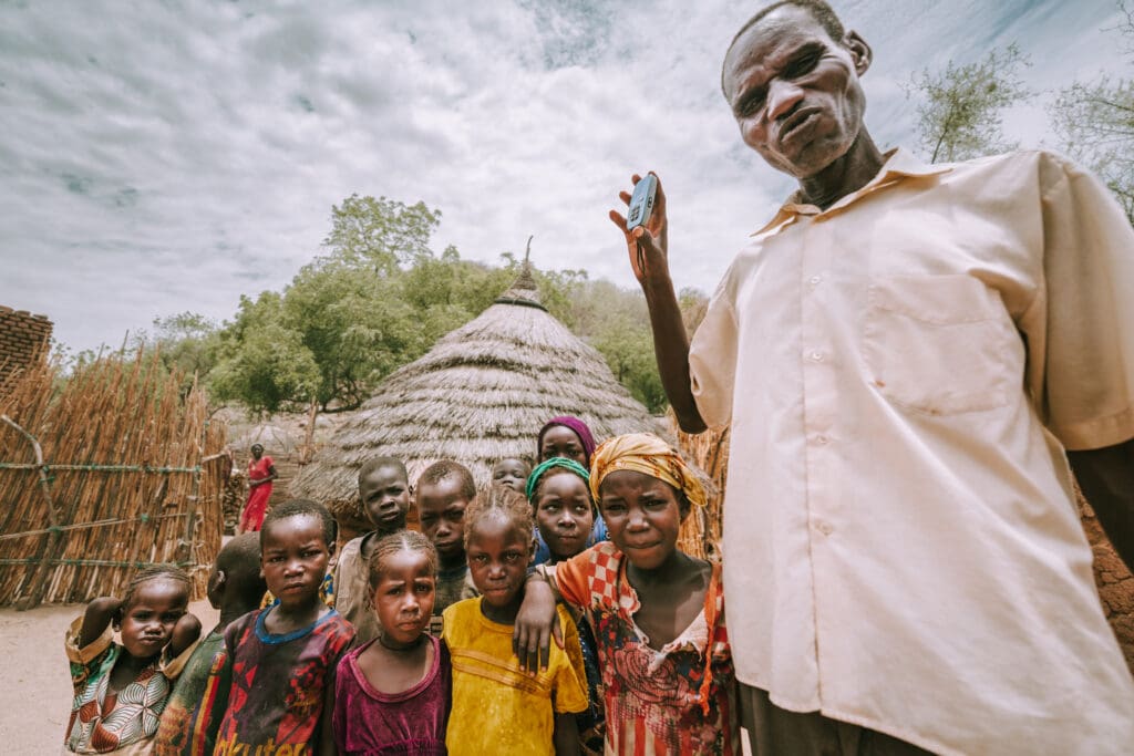 A Chadian father holding an audio Bible surrounded by children and family in his village compound
